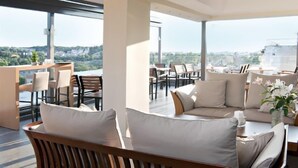 A modern, open-plan living area with a large window offering a city view. There are seating arrangements including a sofa and chairs. - A for Athens (Athens)