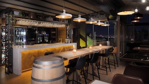 A bar area with a wooden counter, bar stools, and hanging pendant lights. - A for Athens (Athens)