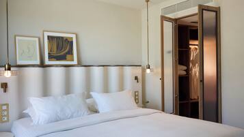 A hotel room with a neatly made bed, a bedside table, a wall-mounted light, and a wardrobe with a mirror.