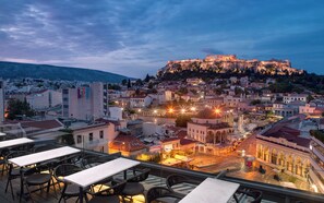 A rooftop terrace with tables and chairs overlooking a historic cityscape with a prominent hilltop fortress. - A for Athens (Athens)