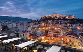 Terraza en la azotea con mesas y sillas con vistas a un paisaje urbano histórico y una fortaleza imponente en la cima de una colina.