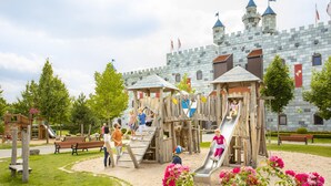 A castle-themed playground with slides and climbing structures, surrounded by benches and a castle facade in the background. - LEGOLAND Feriendorf (Guenzburg)