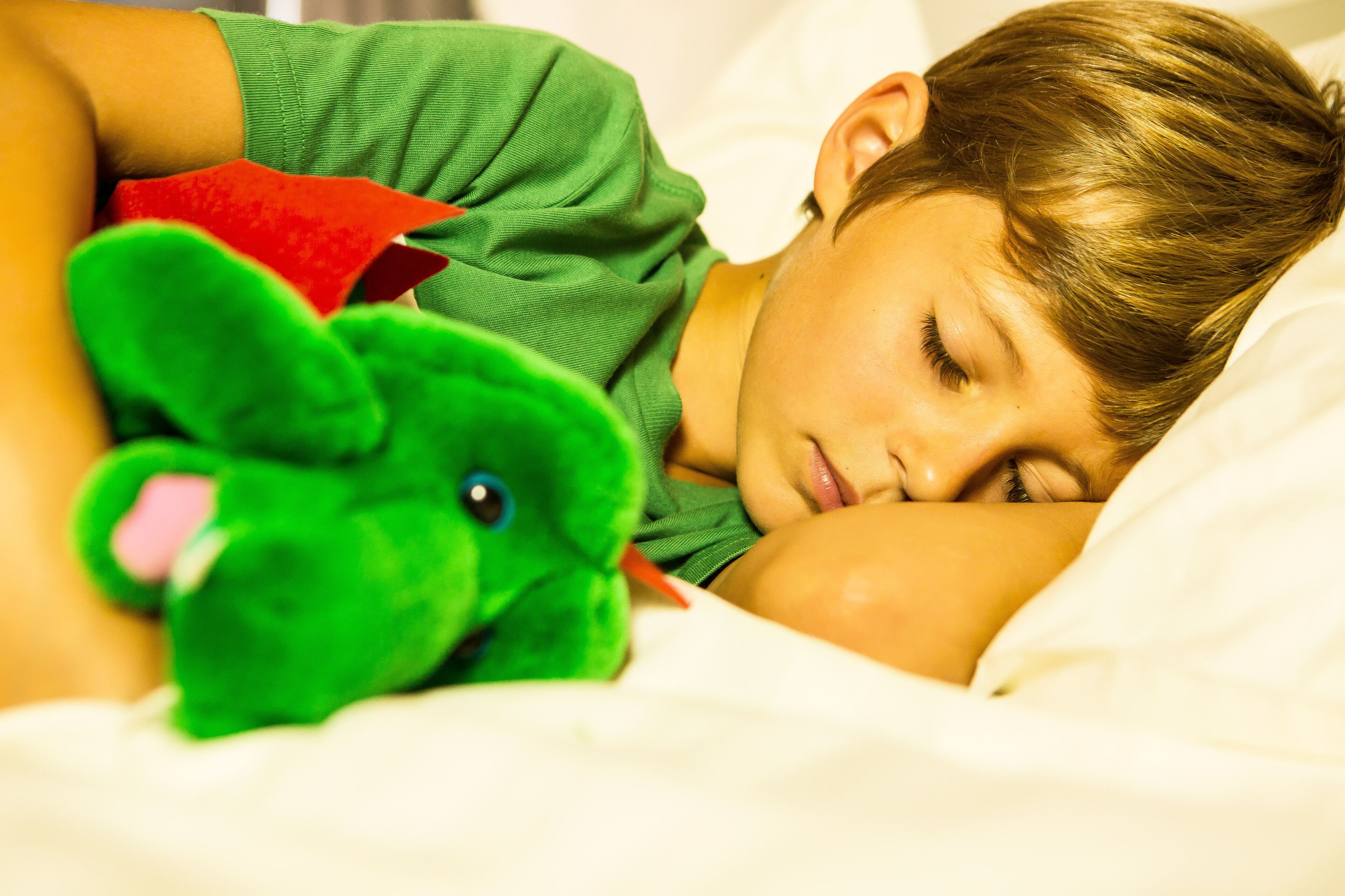 Una persona sdraiata su un letto con un peluche verde.