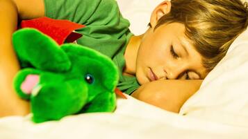 Una persona sdraiata su un letto con un peluche verde.