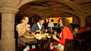 Un restaurant aux arches de pierre et aux poutres en bois, avec des tables garnies d’assiettes de nourriture et de verres de vin, et une ambiance chaleureuse et accueillante.