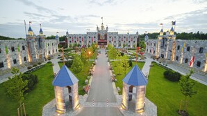 Une structure ressemblant à un château, dotée de plusieurs tours, d’une entrée principale et d’un jardin bien entretenu.