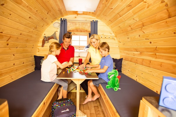 A family of four in a wooden cabin with a table, toys, and a sleeping area. - LEGOLAND Feriendorf (Guenzburg)