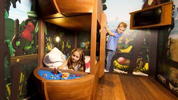 A play area with a wooden boat, jungle-themed murals, and a television on a wooden stand.