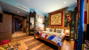 Une chambre avec un lit en bois, une table de chevet, une fresque murale et une petite table pour les jouets.