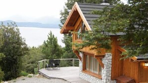 A cabin with a stone exterior, wooden deck, and a view of a lake. - Las Morillas Huemul Lodge (Nahuel Huapi National Park)