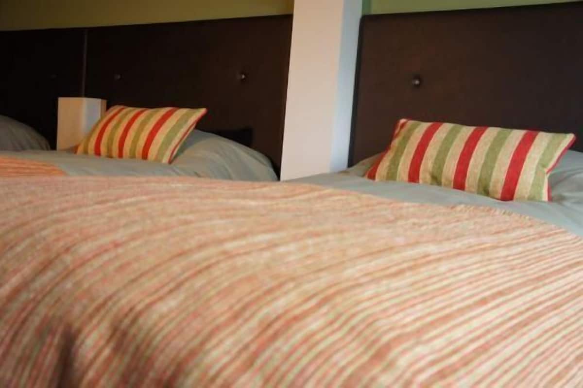 A hotel room with two beds, each with striped bedding and a dark headboard.