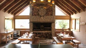 A dining area with a stone fireplace, wooden tables, and benches. - Las Morillas Huemul Lodge (Nahuel Huapi National Park)