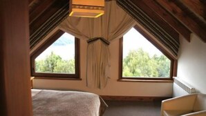 A bedroom with a bed, a chair, and two windows with curtains. - Las Morillas Huemul Lodge (Nahuel Huapi National Park)