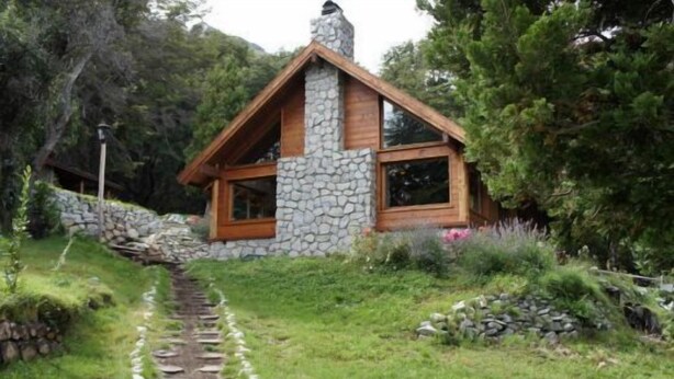 A rustic cabin with a stone chimney, wooden windows, and a stone pathway leading to it. - Las Morillas Huemul Lodge (Nahuel Huapi National Park)