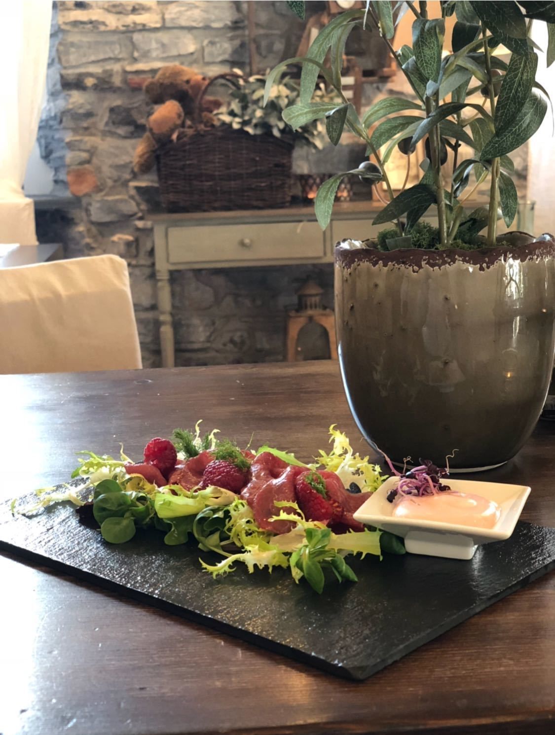 Uma mesa de jantar com um tabuleiro de ardósia preta, um prato de comida e um vaso de planta.