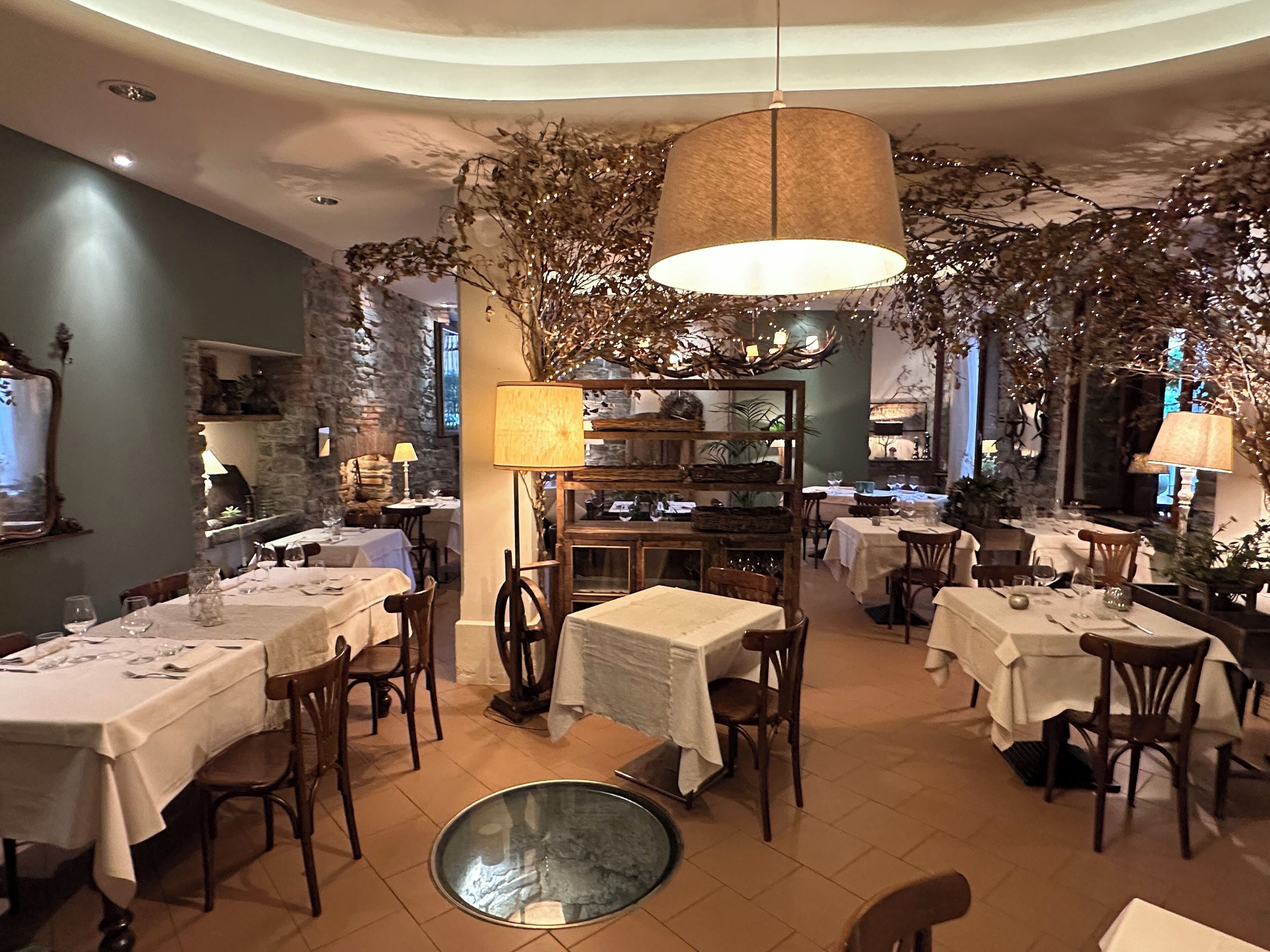 Un ristorante con diversi tavoli e sedie, un lampadario al centro e decorazioni vegetali.