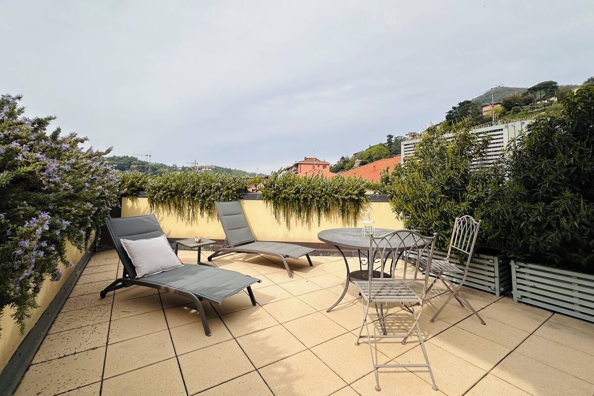 A rooftop terrace with lounge chairs, a table, and a hanging plant arrangement.