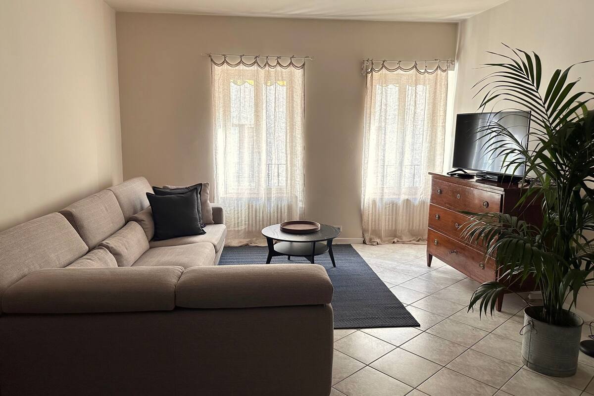 A living room with a sofa, a small round table, a television on a wooden cabinet, and a potted plant.