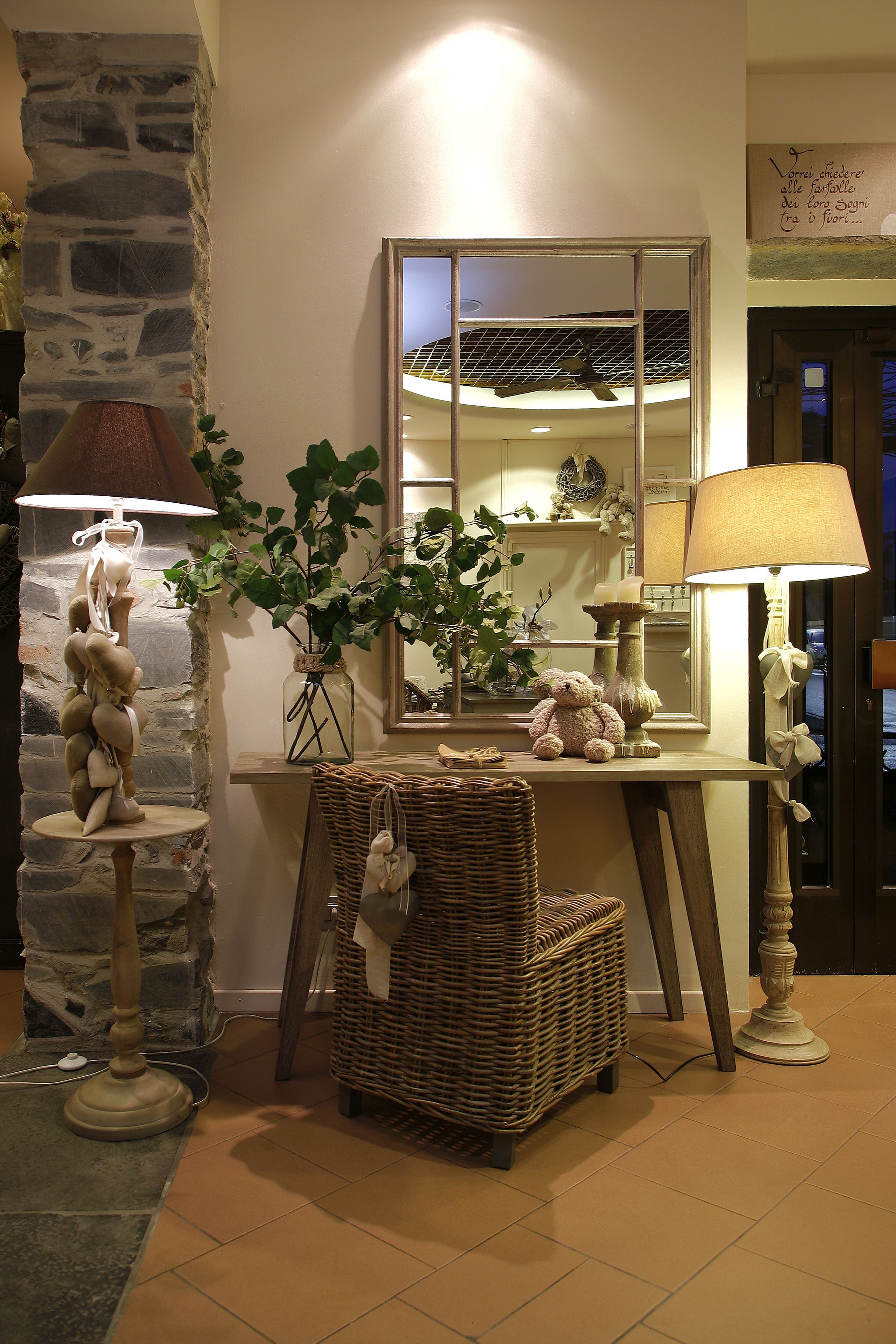 A cozy room with a stone wall, a wicker chair, a mirror, and a lamp.