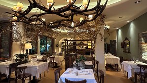 A restaurant with tables set for dining, a chandelier with antler branches, and a view of the dining area. - Hotel San Giuseppe (Cernobbio)