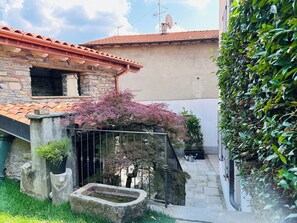 A courtyard with a stone wall, a small fountain, and a tree with pink leaves. - Hotel San Giuseppe (Cernobbio)