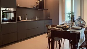 A modern kitchen with dark cabinetry, a built-in oven, and a dining area with a table set for two. - Hotel San Giuseppe (Cernobbio)
