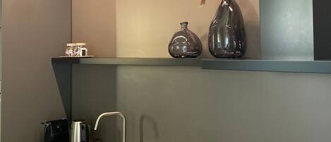 A modern kitchen with a stainless steel sink, a kettle, and a vase with a plant.