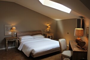 Une chambre à coucher avec un puits de lumière, un lit, deux tables de chevet avec des lampes, une chaise et un bureau avec une lampe.