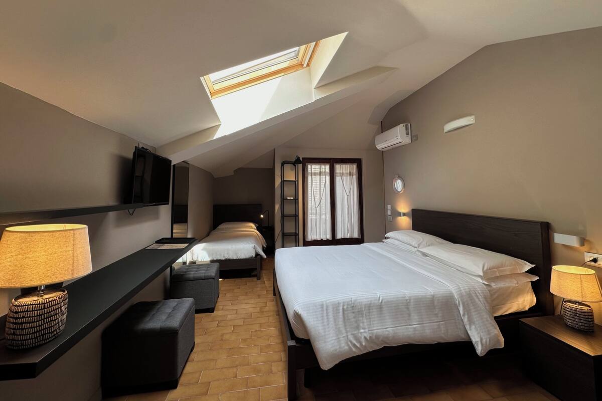 A hotel room with a skylight, a bed, a desk with a lamp, a TV, and a small seating area.