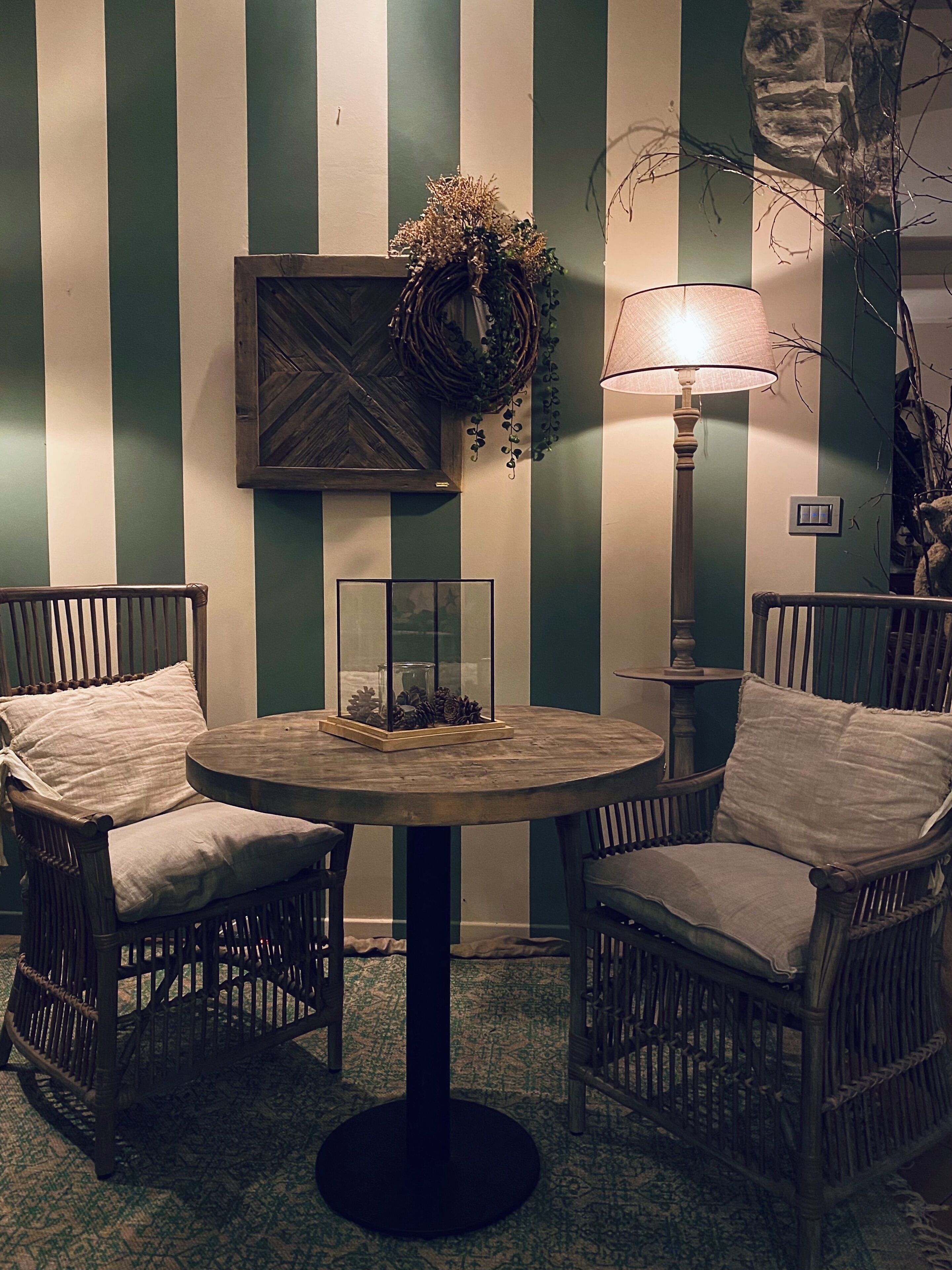 A room with striped walls, wicker chairs, a round table, a lamp, and a decorative wreath.