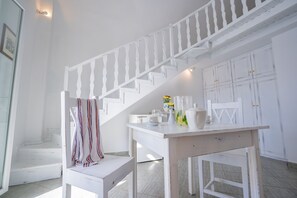 A white staircase with a railing, a wooden bench, a table with a vase of flowers, and white cabinets. - Milos Villas (Santorini)