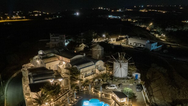 An aerial view of a resort with a swimming pool, a windmill, and a large water tank. - Milos Villas (Santorini)