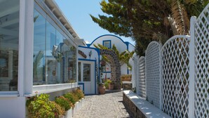 A narrow cobblestone pathway leading to a building with large windows and a blue and white facade. - Milos Villas (Santorini)