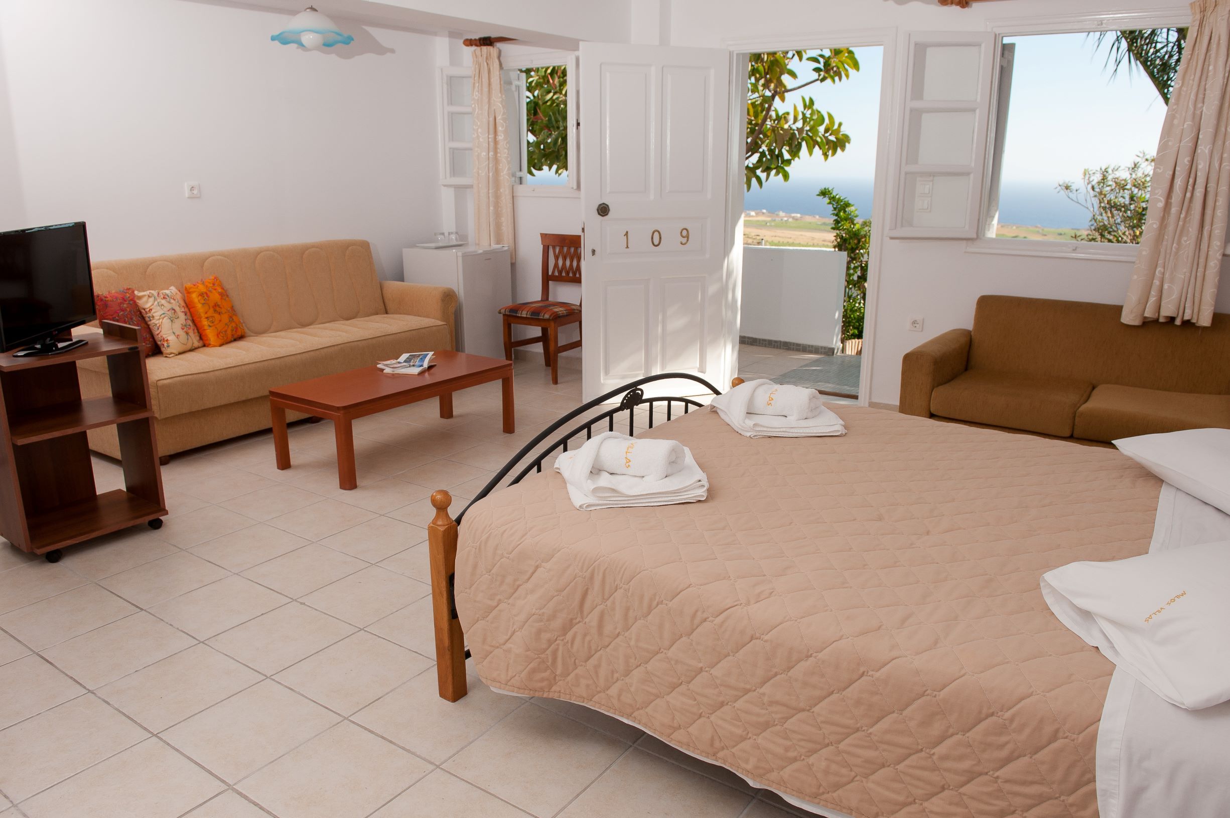 A hotel room with a bed, two sofas, a TV, and a balcony with a view.