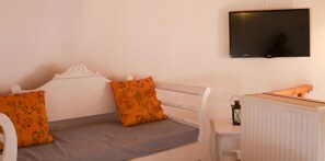 A single bed with two pillows, a bedside table with a lantern, and a television mounted on the wall. - Milos Villas (Santorini)