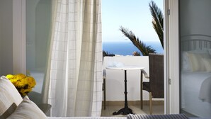 A hotel room with a bed, a small table, and a view of the ocean. - Milos Villas (Santorini)