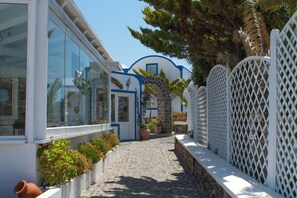 A narrow cobblestone path leading to a building with large windows and a blue and white facade. - Milos Villas (Santorini)