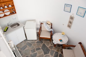 Cocina compacta con pileta, refrigerador y estantes de madera. Hay un pequeño comedor con una silla y una mesa, además de un objeto decorativo en la pared.