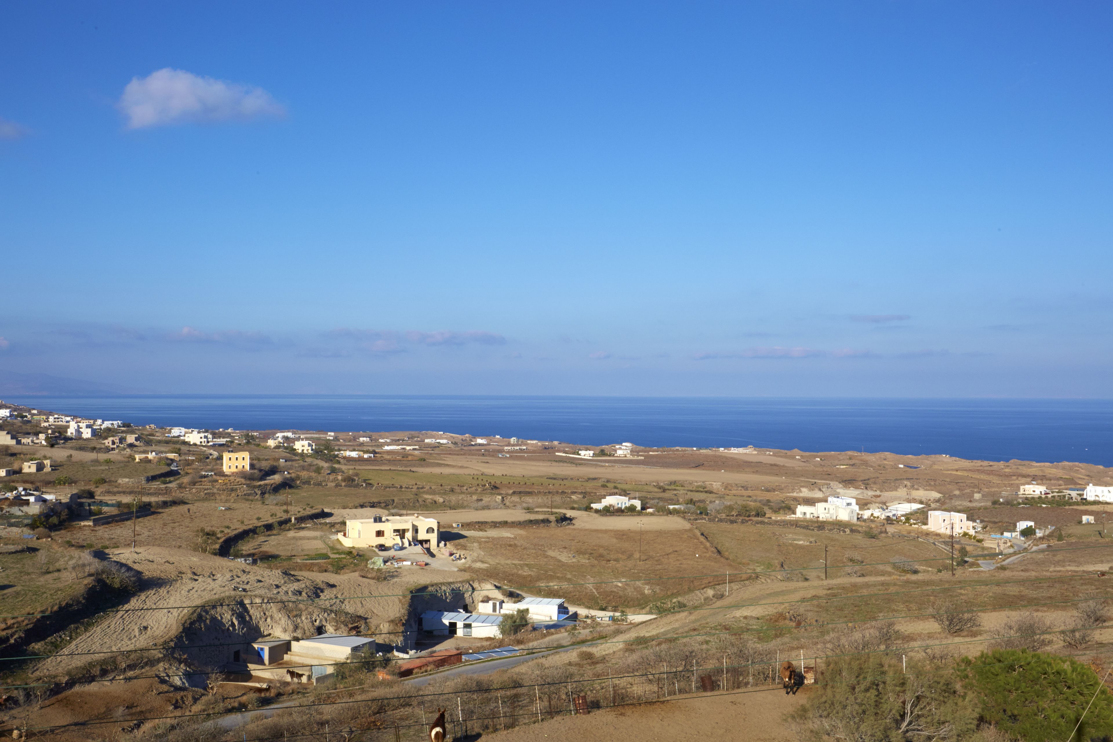 A coastal village with scattered buildings, a clear sky, and the sea in the background.