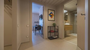 A hallway leading to a dining area with a TV mounted on the wall, a framed artwork, and a small shelf with a plant. - Centro Siloe Residence Hotel (Milan)