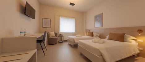 Habitación de hotel con cama, escritorio, silla, mesita, televisor y ventana.