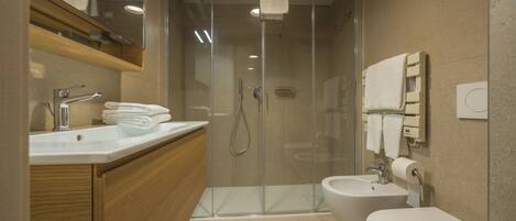 A modern bathroom with a glass-enclosed shower, a sink with a mirror, a bidet, and a toilet.