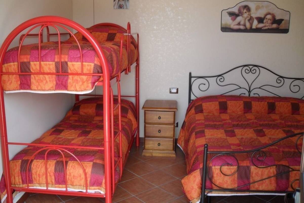 A room with bunk beds and a single bed, a wooden nightstand, and a wall with a picture.