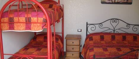 Una habitación con literas y una cama individual, una mesita de noche de madera, y una pared con un cuadro.