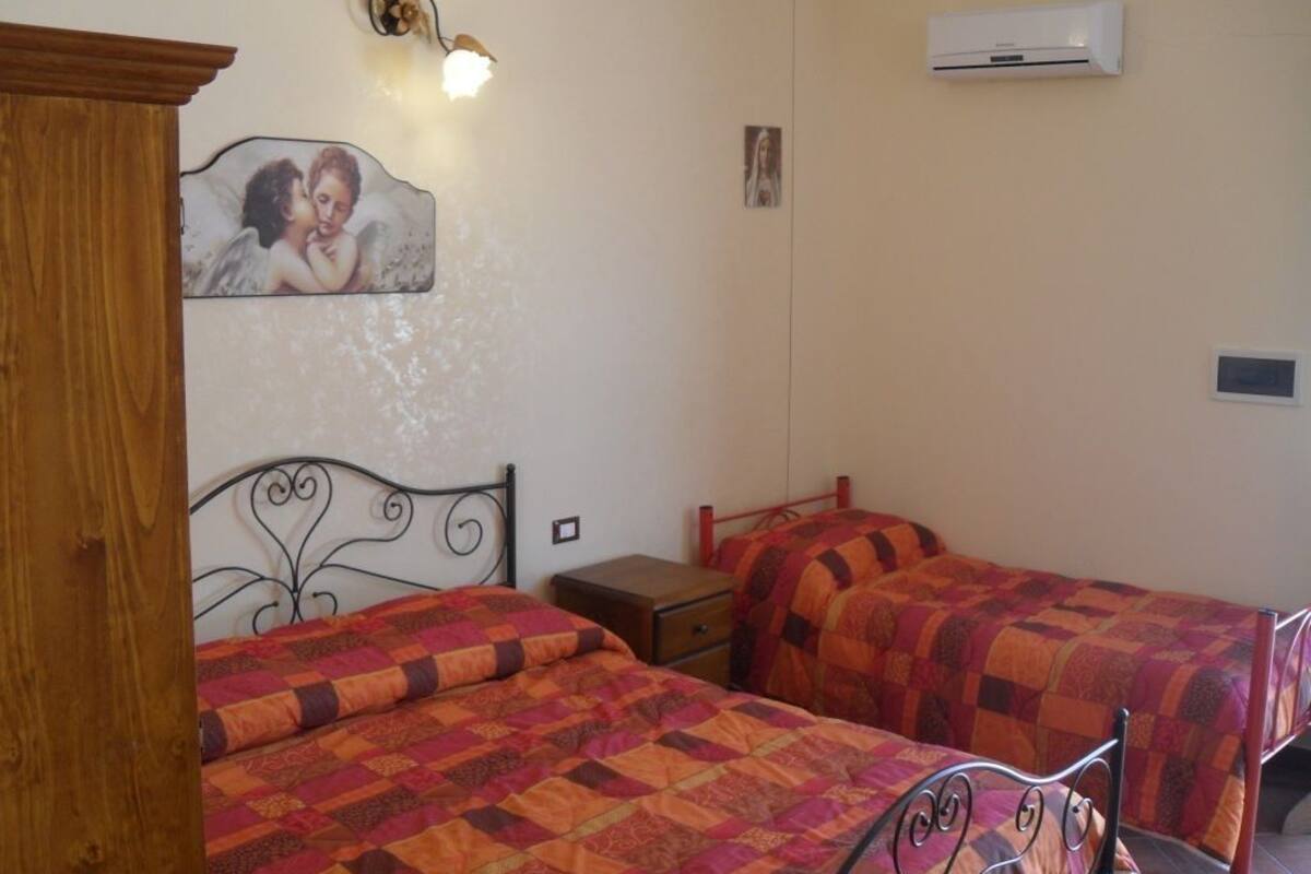 A bedroom with two beds, a wooden wardrobe, a wall-mounted air conditioner, and a decorative angel painting.