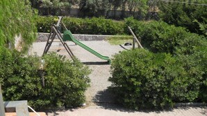 A playground with a green slide and swings, surrounded by dense greenery and a stone wall. - Agriturismo La Targa (Termini Imerese)
