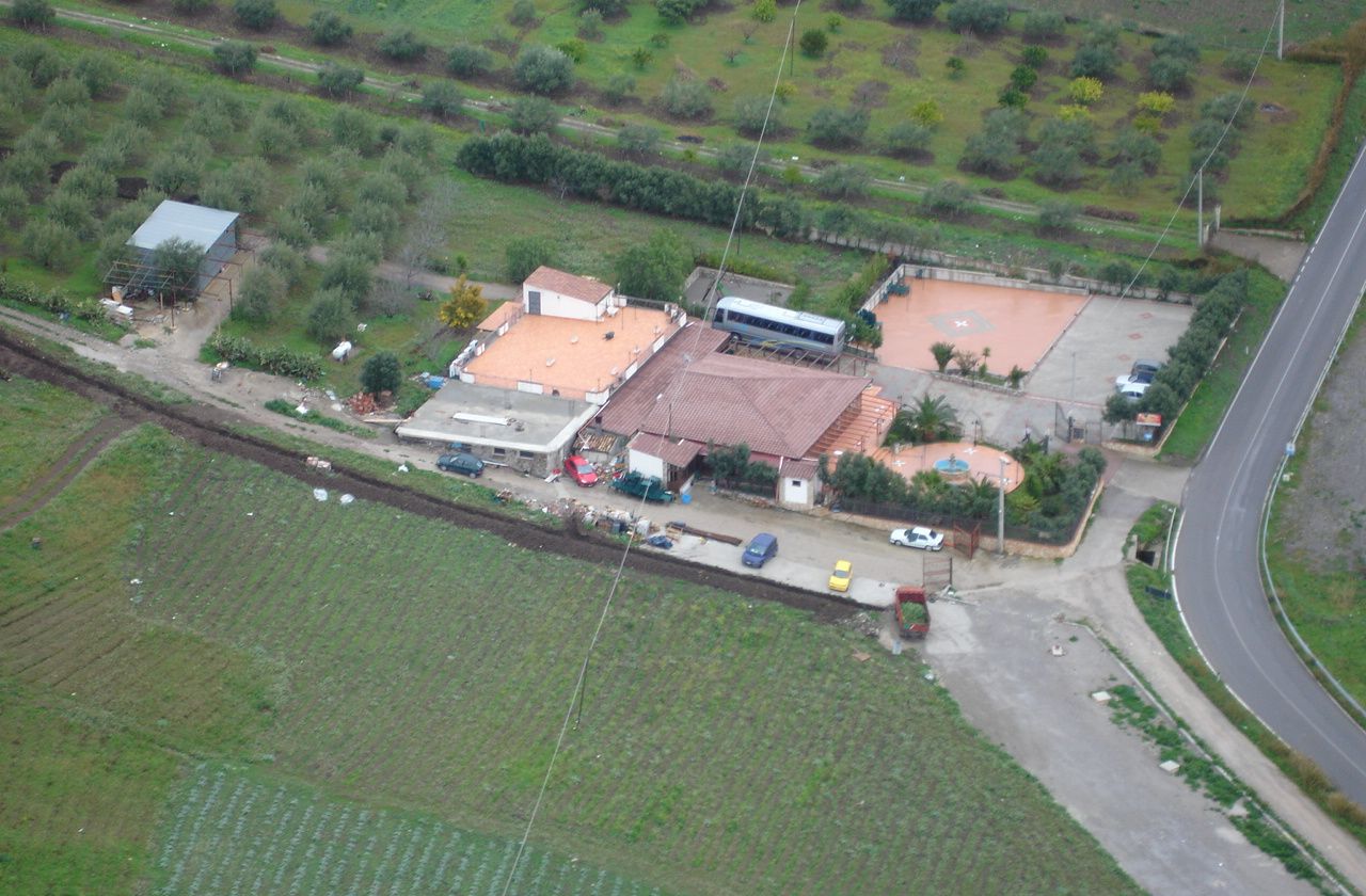 An aerial view of a rural area with agricultural fields, a road, and several buildings including a bus station and a parking lot.