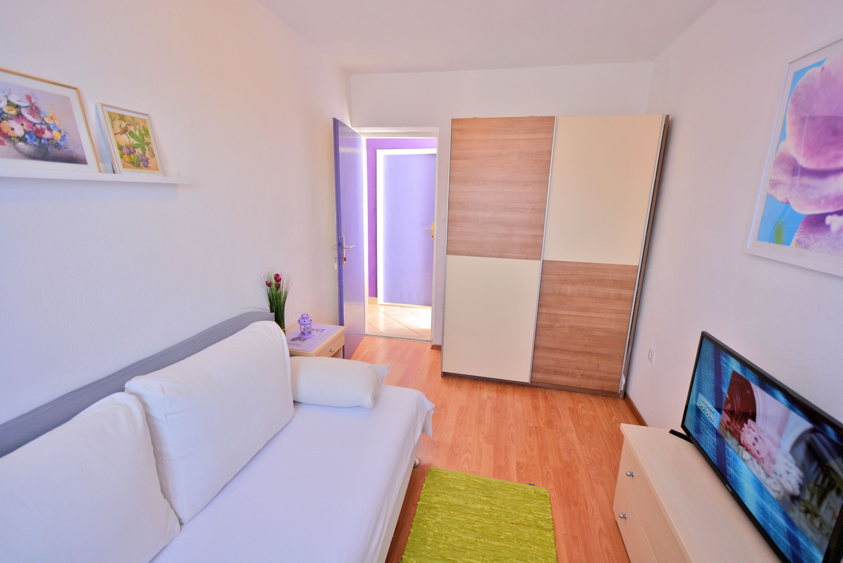 A modern hotel room with a white sofa, a TV, and a wooden wardrobe.
