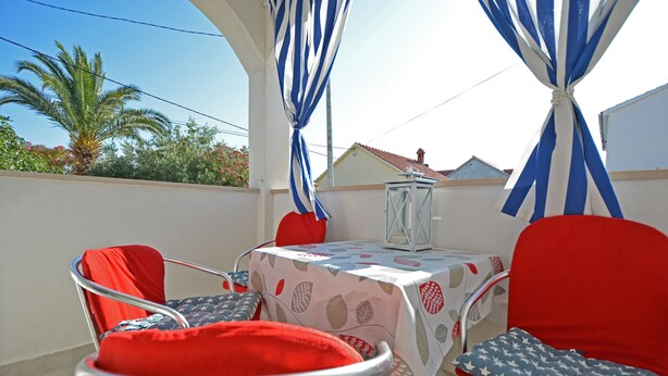 Une terrasse avec une table et des chaises, recouverte d’une nappe blanche ornée d’un motif de feuilles, et agrémentée de rideaux bleus et blancs à rayures.