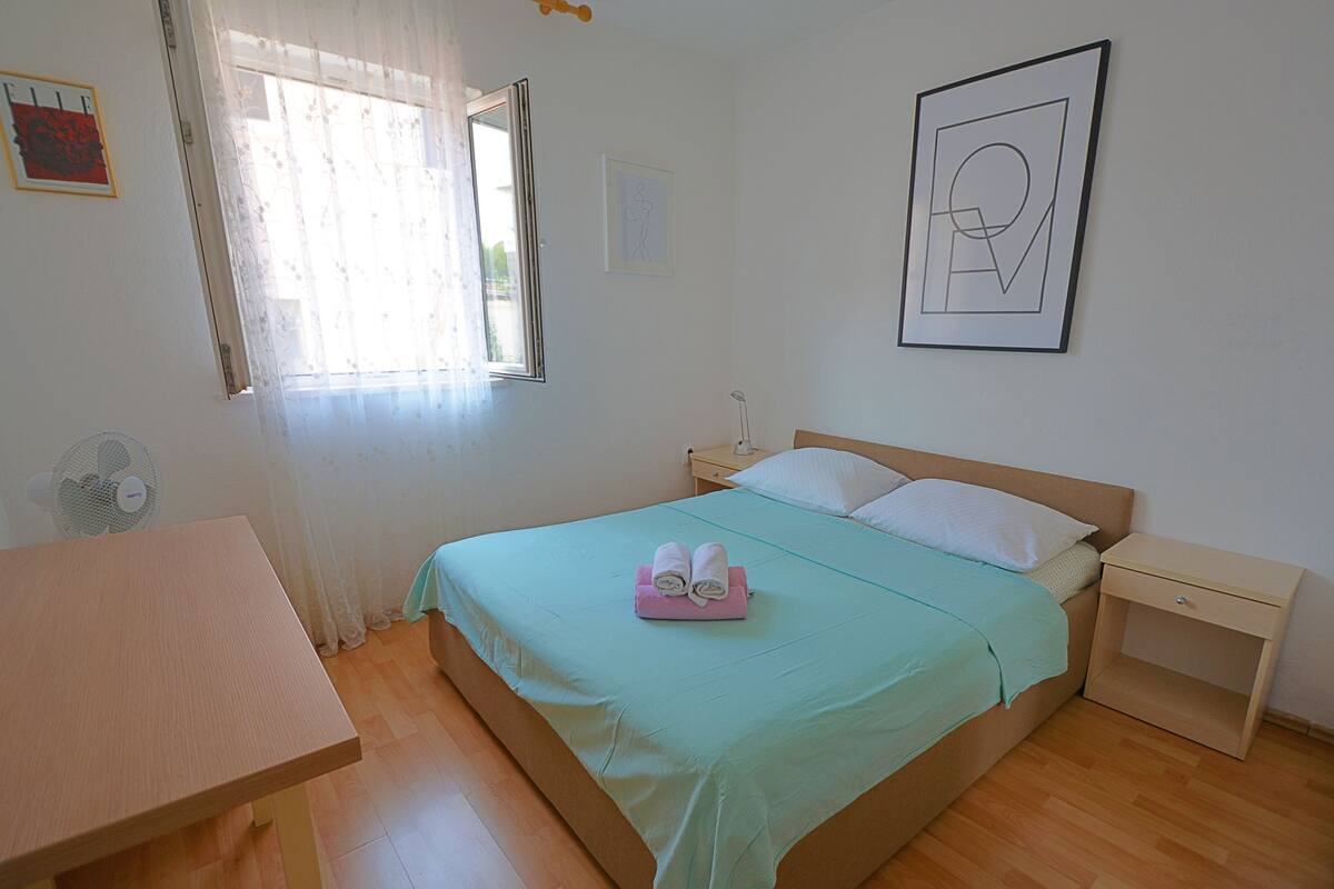 Een slaapkamer met een bed, nachtkastjes, een klein tafeltje en een raam met gordijnen.